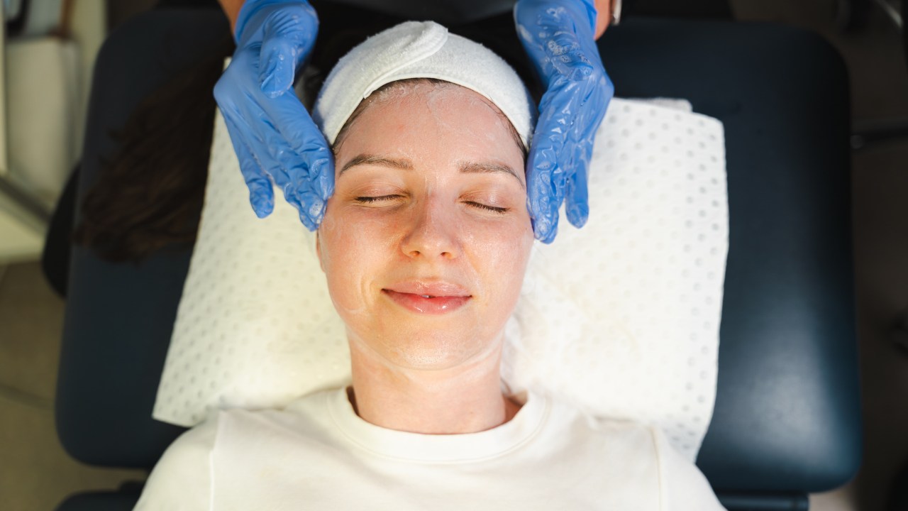 A client lying down relaxing whilst a clinician wearing gloves applies a facial treatment with their hands